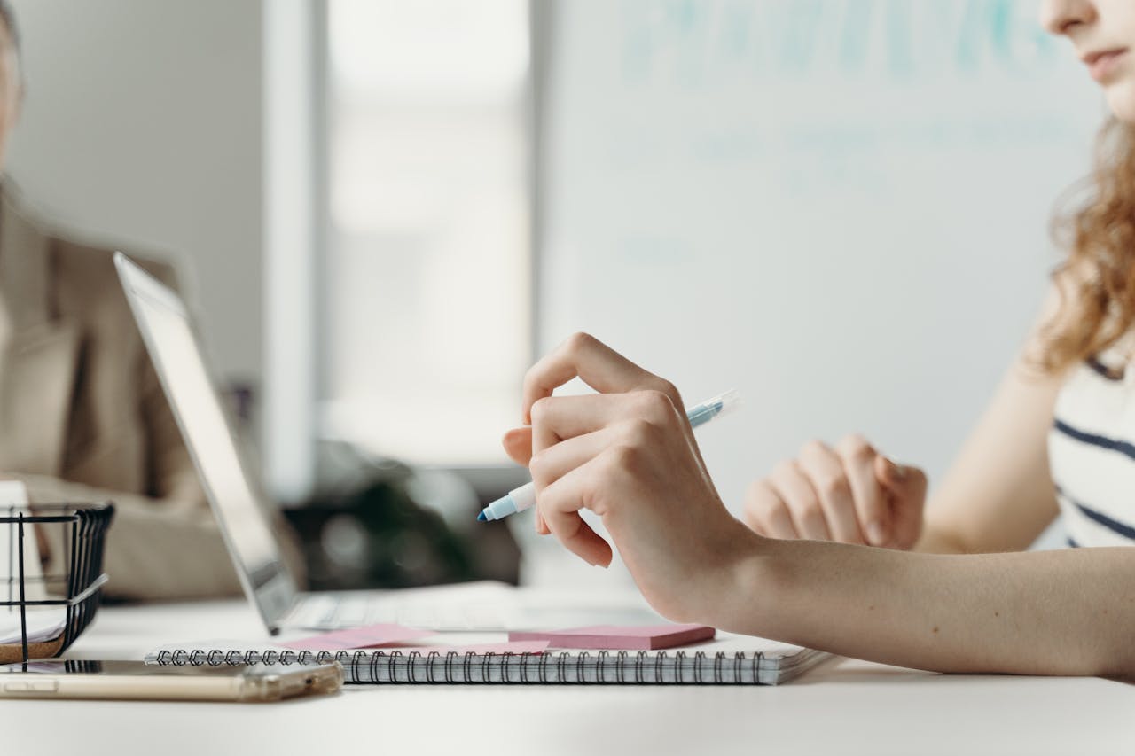 Close-up of a woman in an office, planning on a laptop with notes and pen.